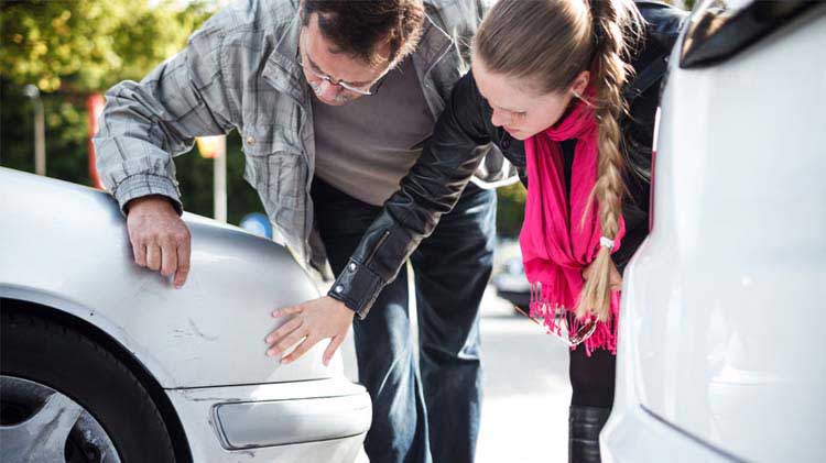 People looking at scratches on a car resulting from car accident.